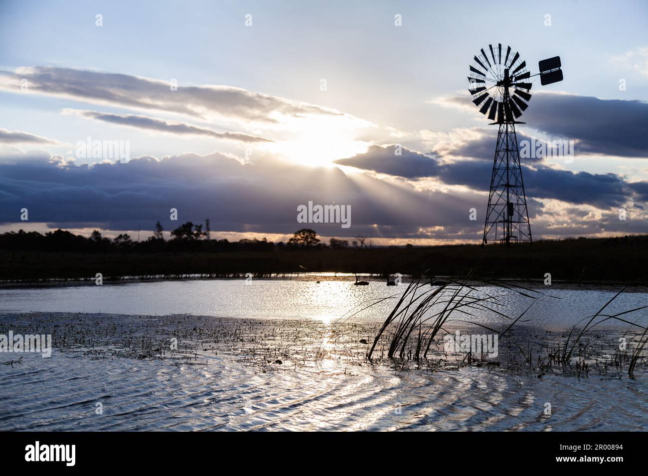 Le soir, la lumière du soleil se brise à travers le nuage sur la ferme australienne avec silhouette de moulin à vent Banque D'Images