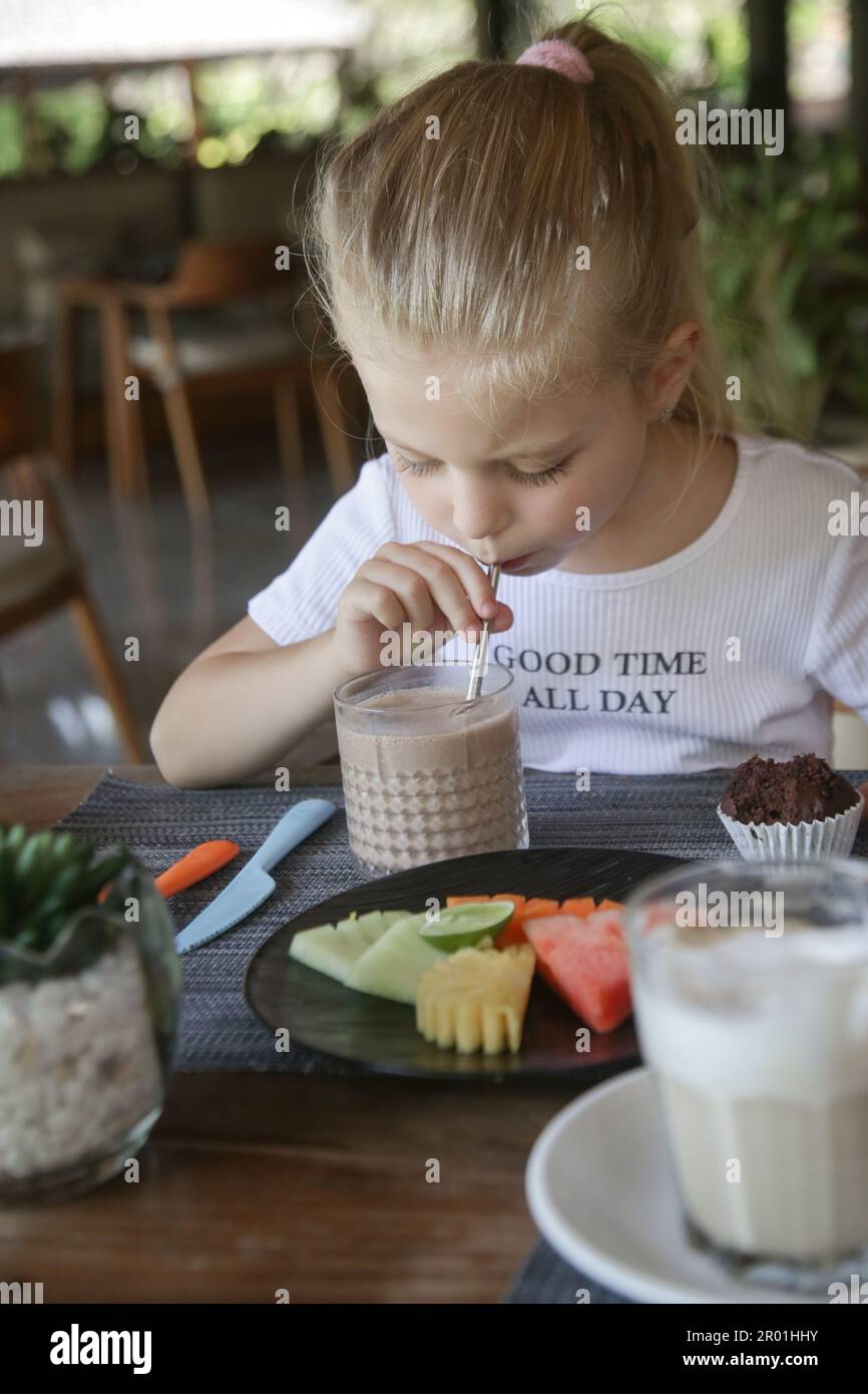 Mignonne fille de 5 ans ayant du lait au chocolat et une assiette de fruits au restaurant Banque D'Images