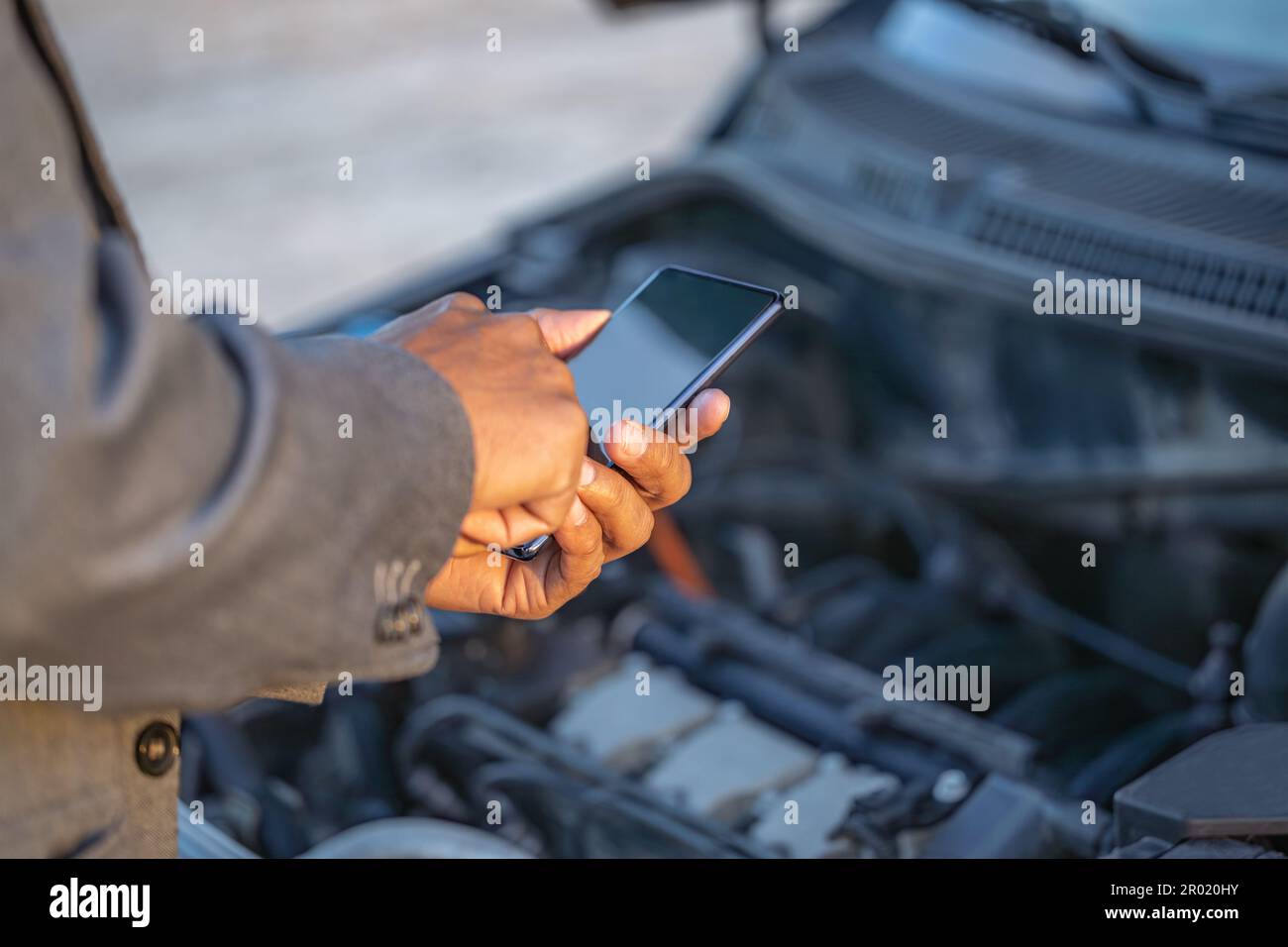 Détail des mains d'un homme Latino avec son téléphone mobile avec sa voiture en panne en arrière-plan. Banque D'Images