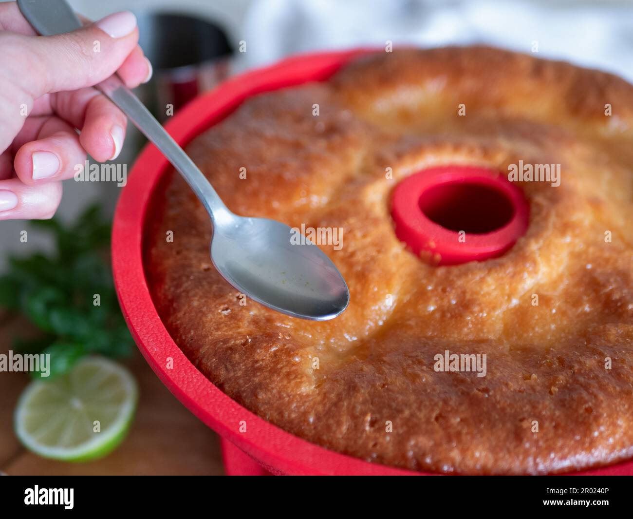 Savarin fraîchement cuit dans moule à gâteau en silicone rouge est versé par sirop, foyer sélectif. Gâteau circulaire imprégné de rhum, gros plan Banque D'Images