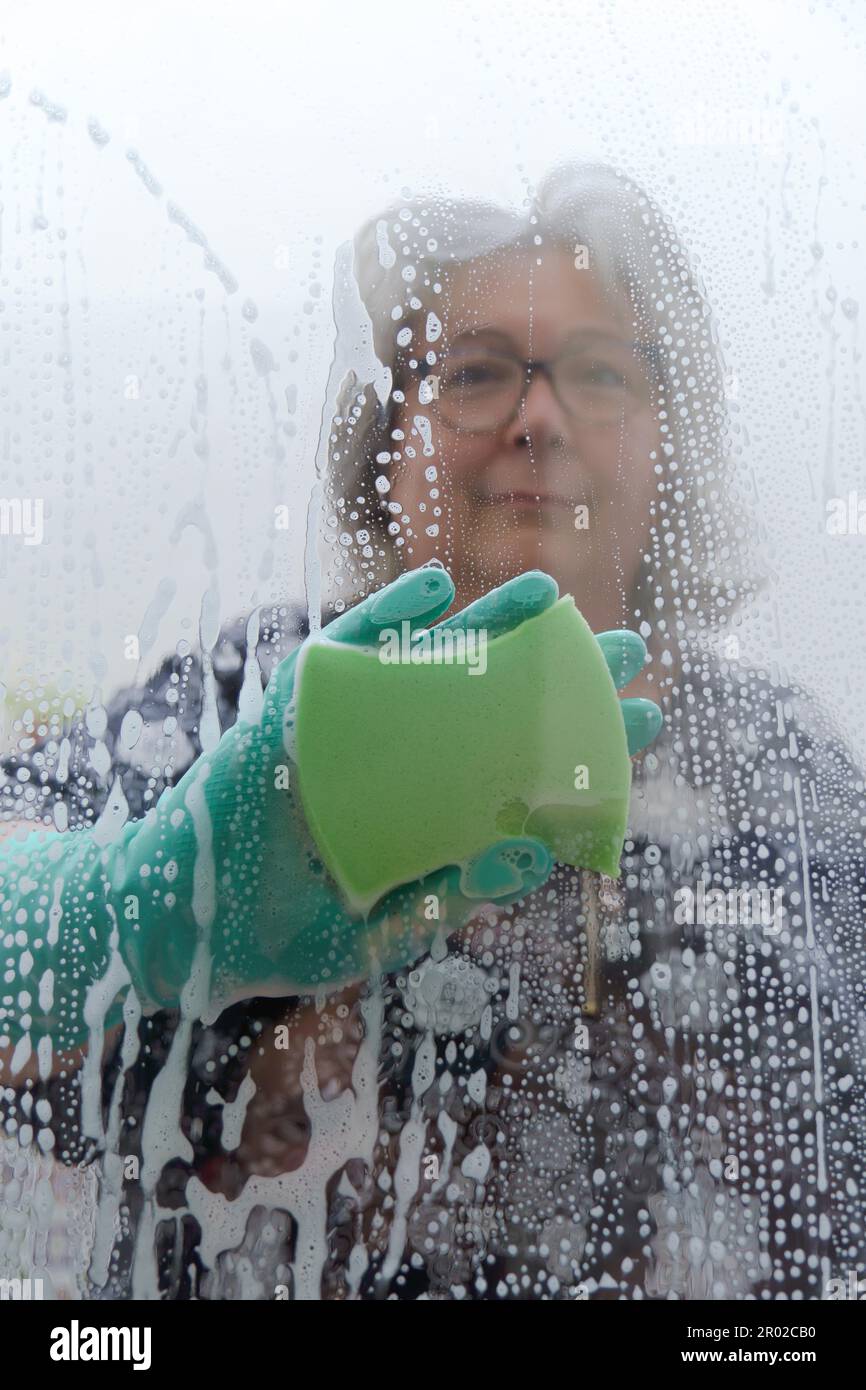 Une femme nettoie le verre avec une éponge verte et des gants Banque D'Images