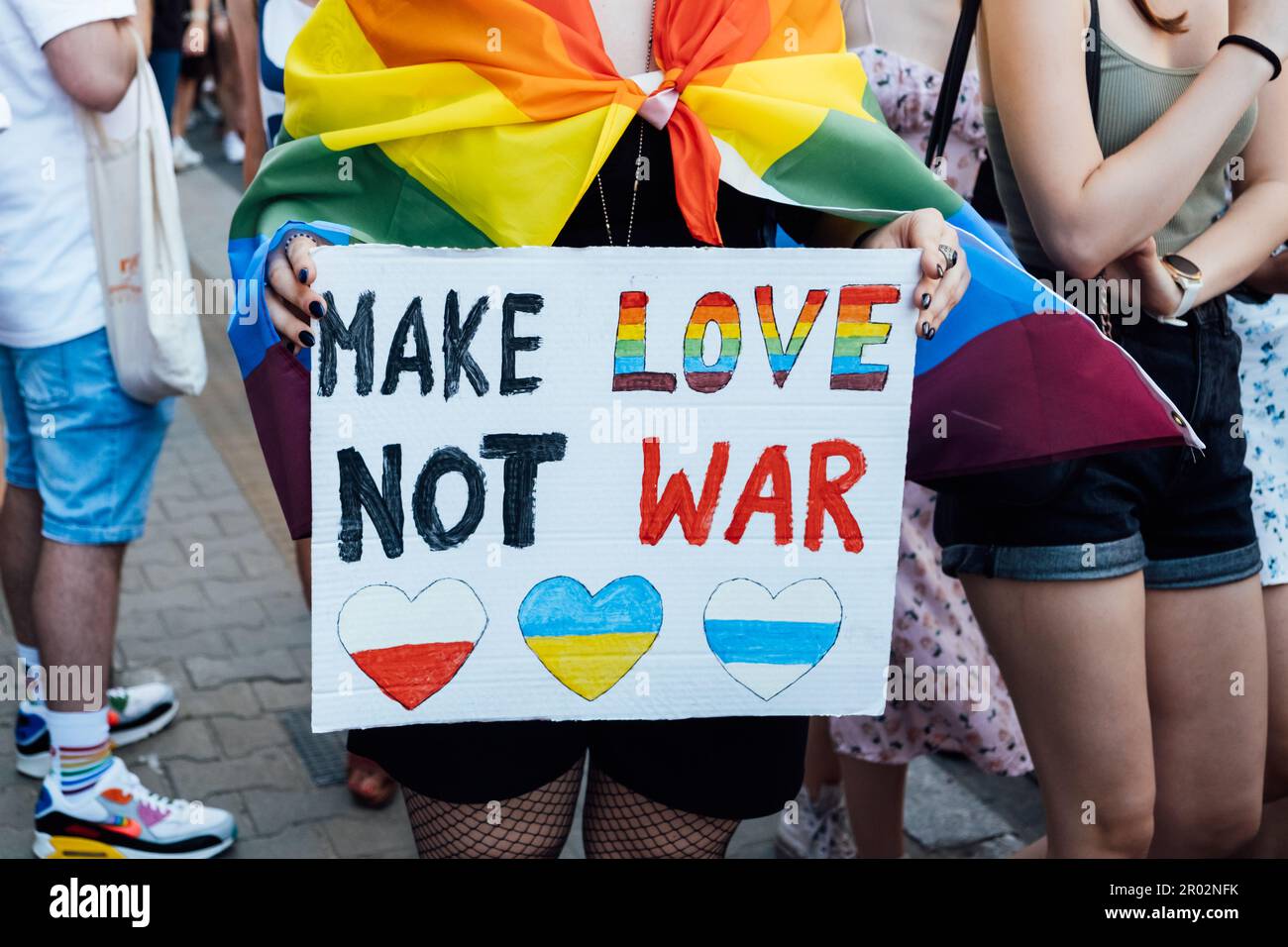 Fierté gay, la marche de solidarité LGBTQ avec des drapeaux arc-en-ciel et des affiches antiguerrières. Les mains tenant une affiche avec font l'amour, pas la guerre Banque D'Images