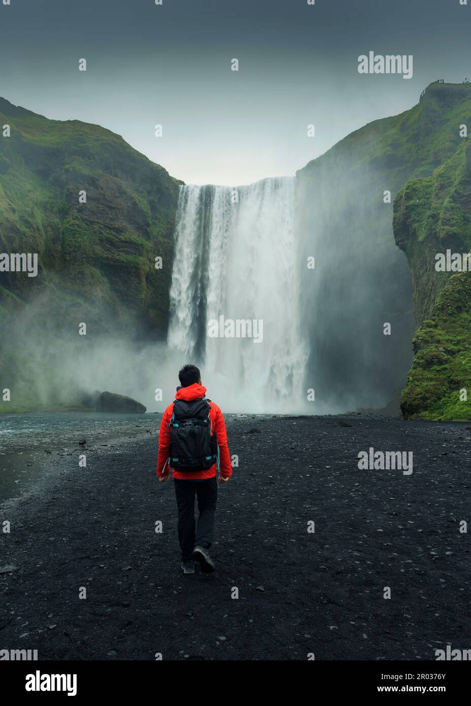 Paysage spectaculaire de la cascade de Skogafoss qui coule avec l'homme asiatique routard marchant en été à l'Islande Banque D'Images
