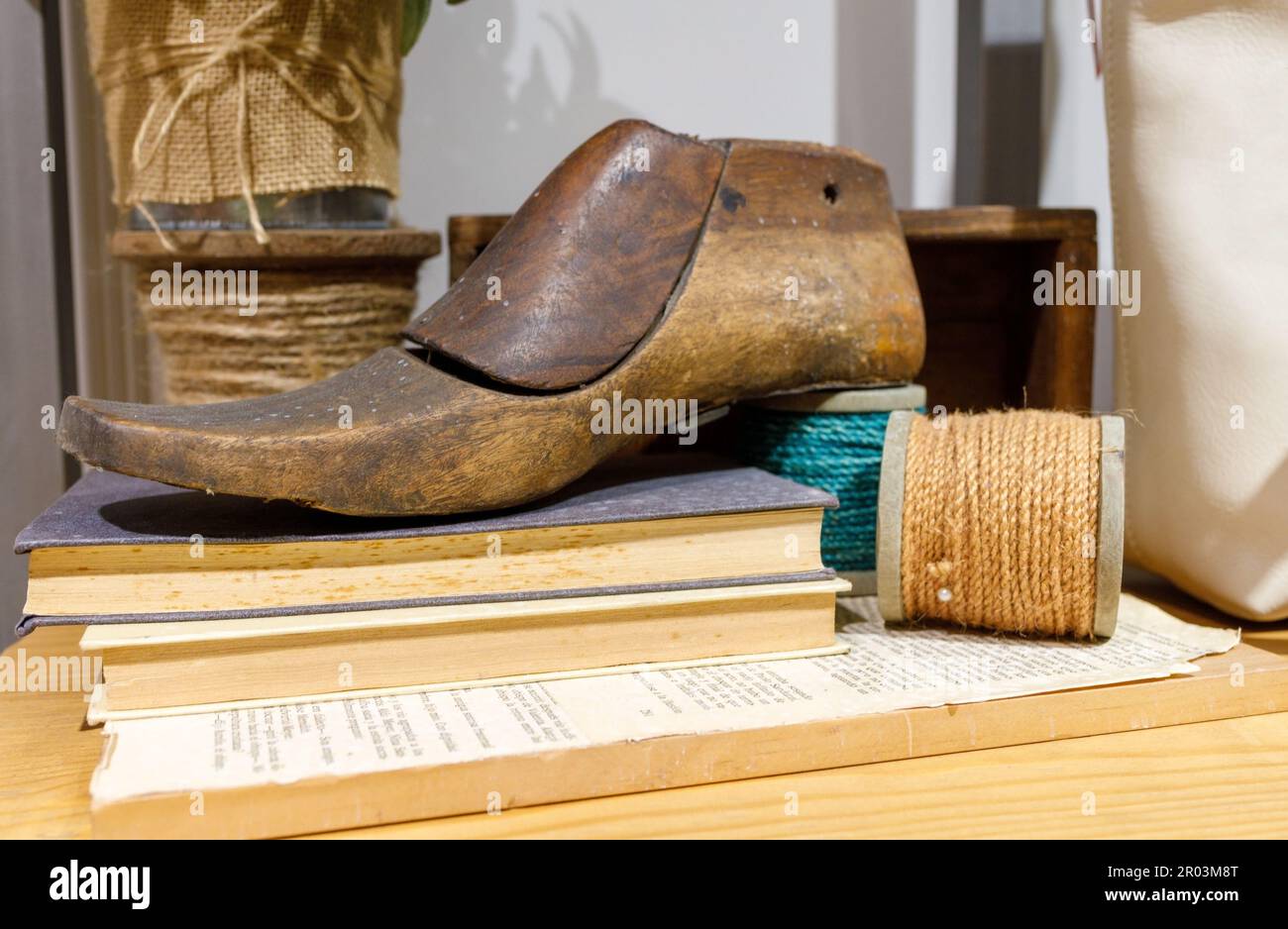 Chaussure en bois posée sur le livre sur la table. Skeins de fil, fabrication de chaussures à la main, atelier, cordonnier, vintage vieux, modèle, maroquinerie, gros Banque D'Images