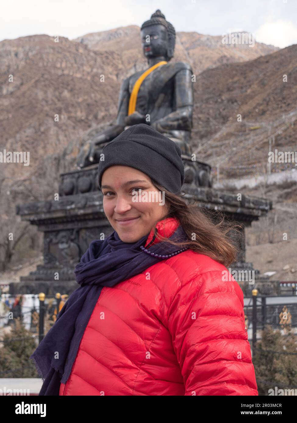 Une femelle Backpacker à Muktinath, au Népal, se répande avec confiance avec un énorme Bouddha de pierre en arrière-plan. Banque D'Images