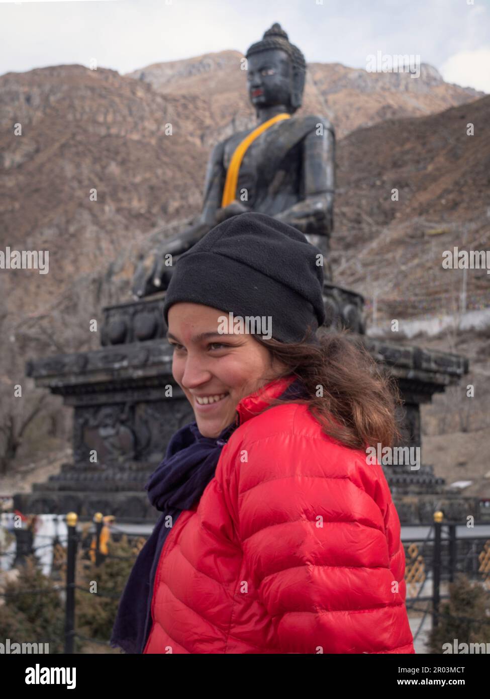 Une femelle Backpacker à Muktinath, Népal, smiling neaky avec un énorme Bouddha de pierre dans le fond. Banque D'Images