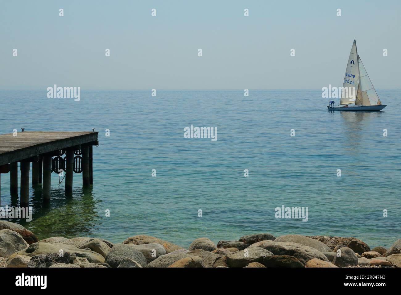 Un petit yacht avec une voile blanche sur le lac de Garde en Italie Banque D'Images