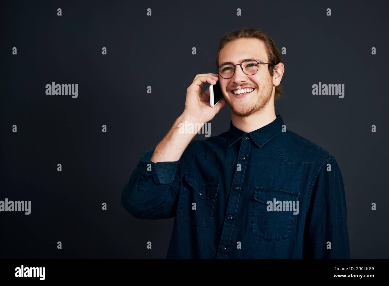 Conclure la vente par téléphone. un beau jeune homme d'affaires debout et parlant sur son téléphone portable sur fond noir dans le studio. Banque D'Images