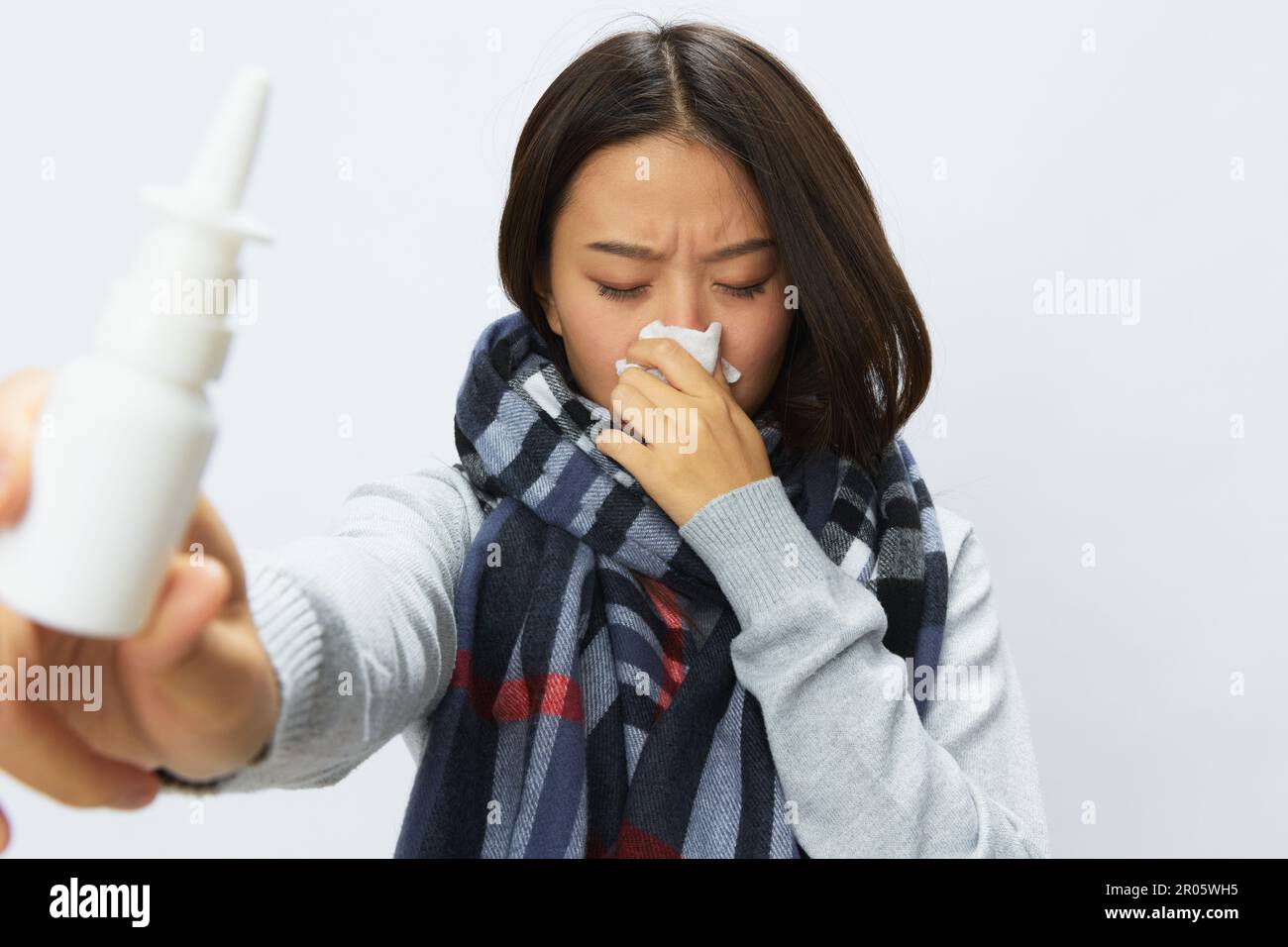 Femme asiatique avec un rhume et un nez bouché tenant un spray nasal pour les allergies avec un mal de gorge portant un foulard à carreaux sur un fond blanc Banque D'Images