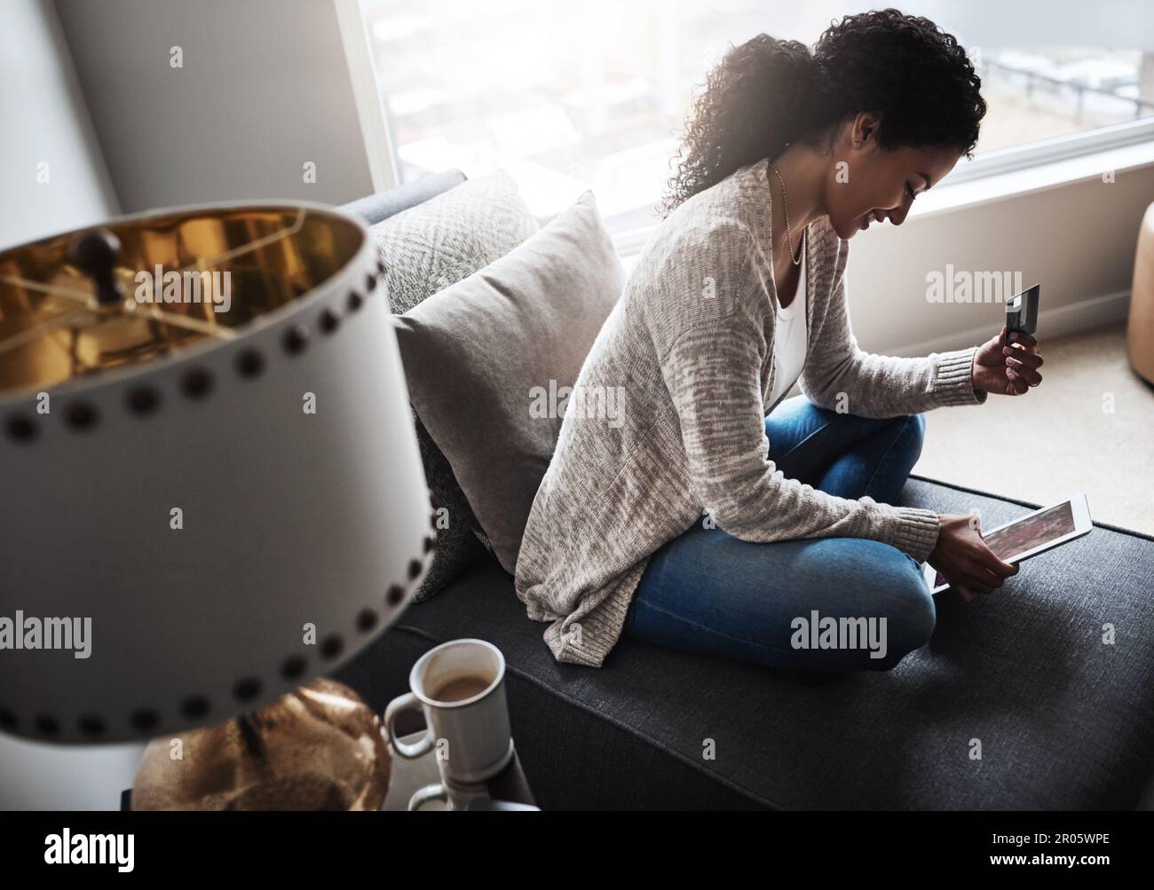 Shopping dans le confort de la maison. une jeune femme joyeuse se détendant sur une chaise tout en faisant des achats en ligne sur une tablette numérique à la maison. Banque D'Images