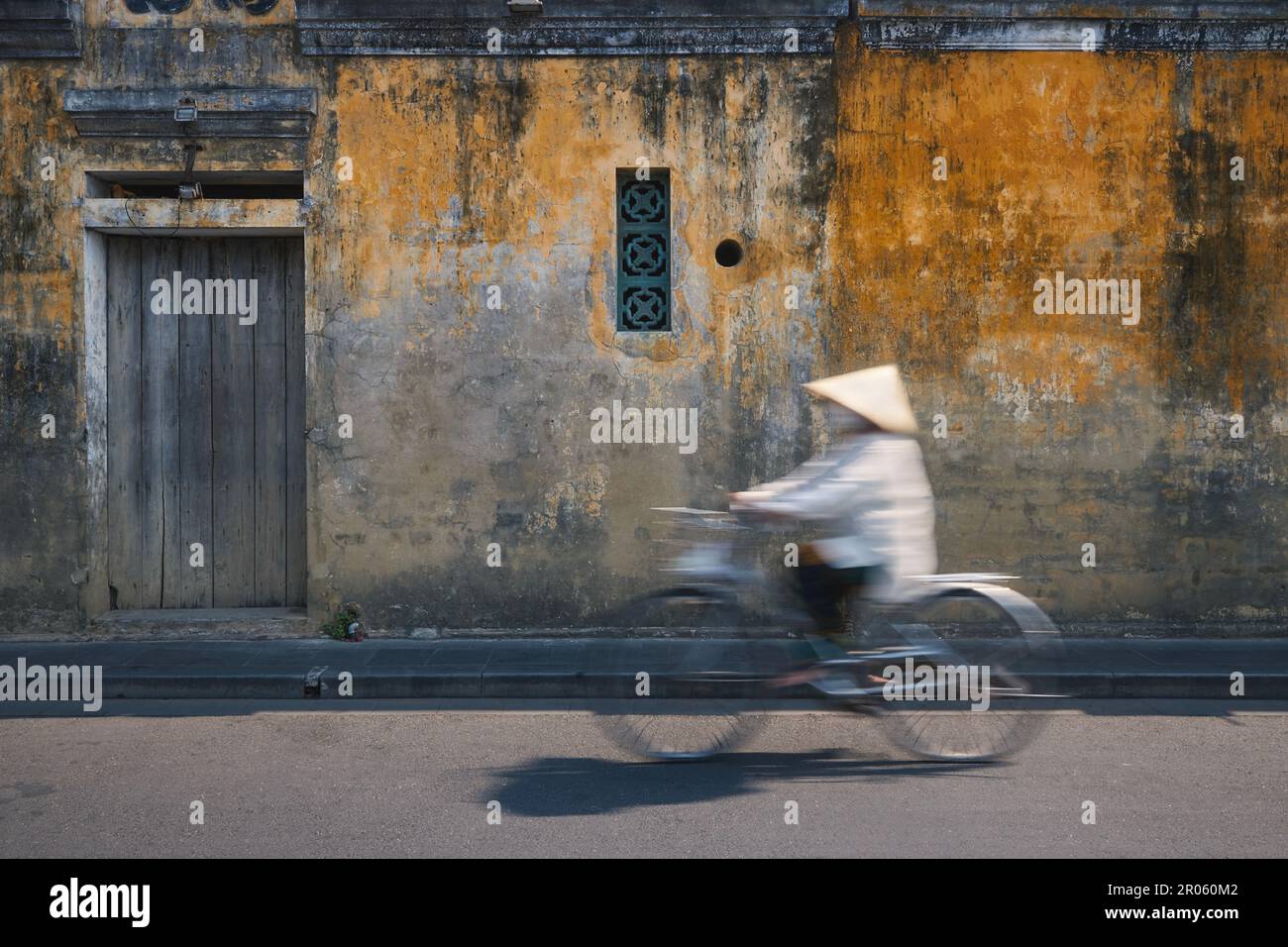 Femme vietnamienne avec chapeau traditionnel à vélo dans la vieille ville. Ville de Hoi an, Vietnam. Banque D'Images