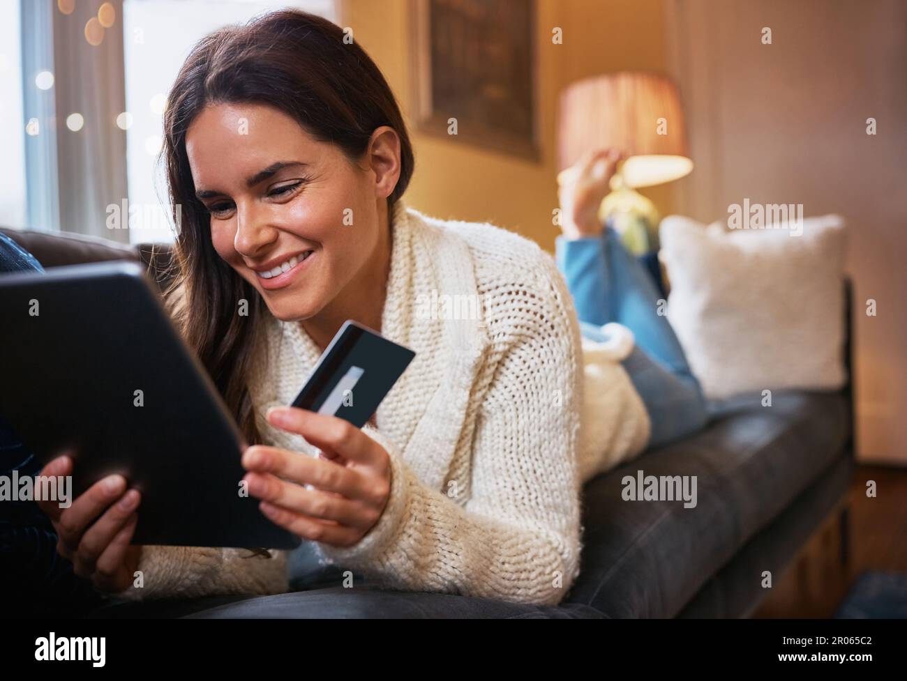 Confort et traitement au détail combinés. une jeune femme attrayante utilisant une tablette numérique et une carte de crédit sur le canapé à la maison. Banque D'Images