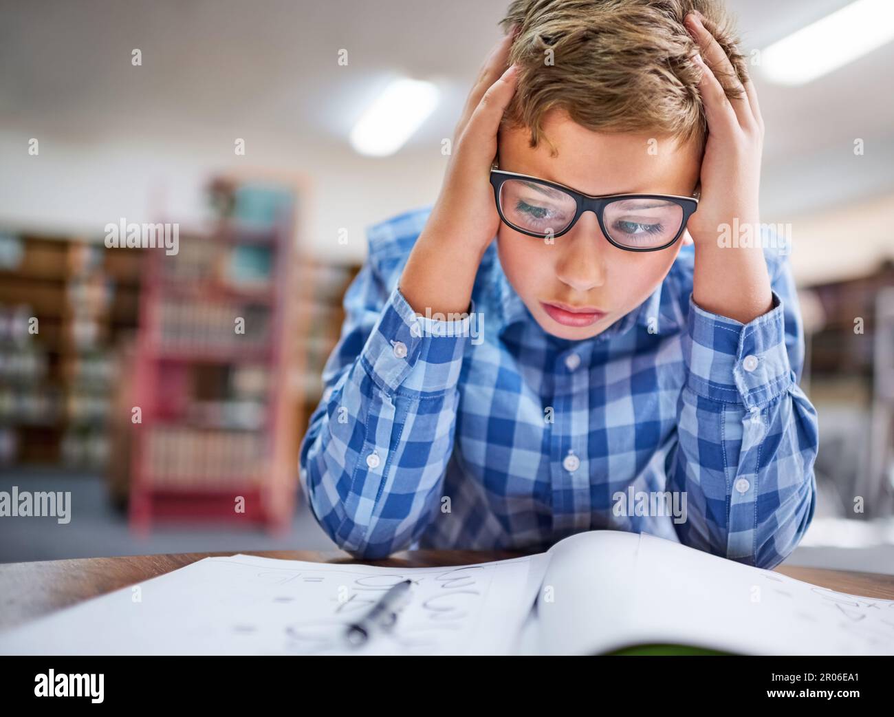 Je suis tellement confus... un jeune garçon qui regarde stressé pendant qu'il travaille en classe à l'école. Banque D'Images