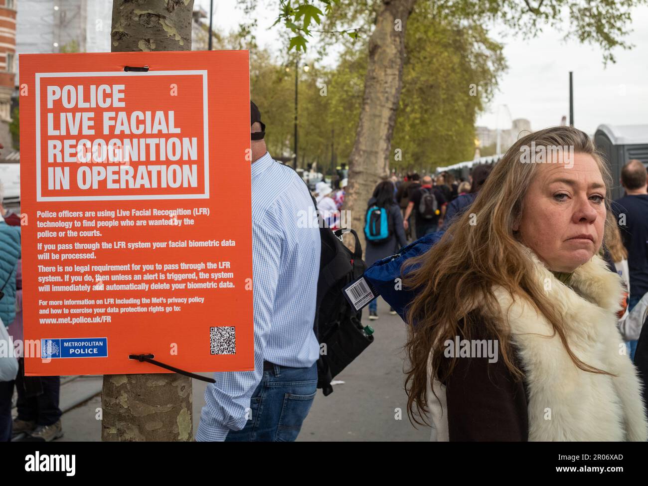 Couronnement, Londres, le 6 mai 2023. Une femme regarde directement la caméra à côté d'un panneau de la police métropolitaine de Londres annonçant l'utilisation de live f Banque D'Images