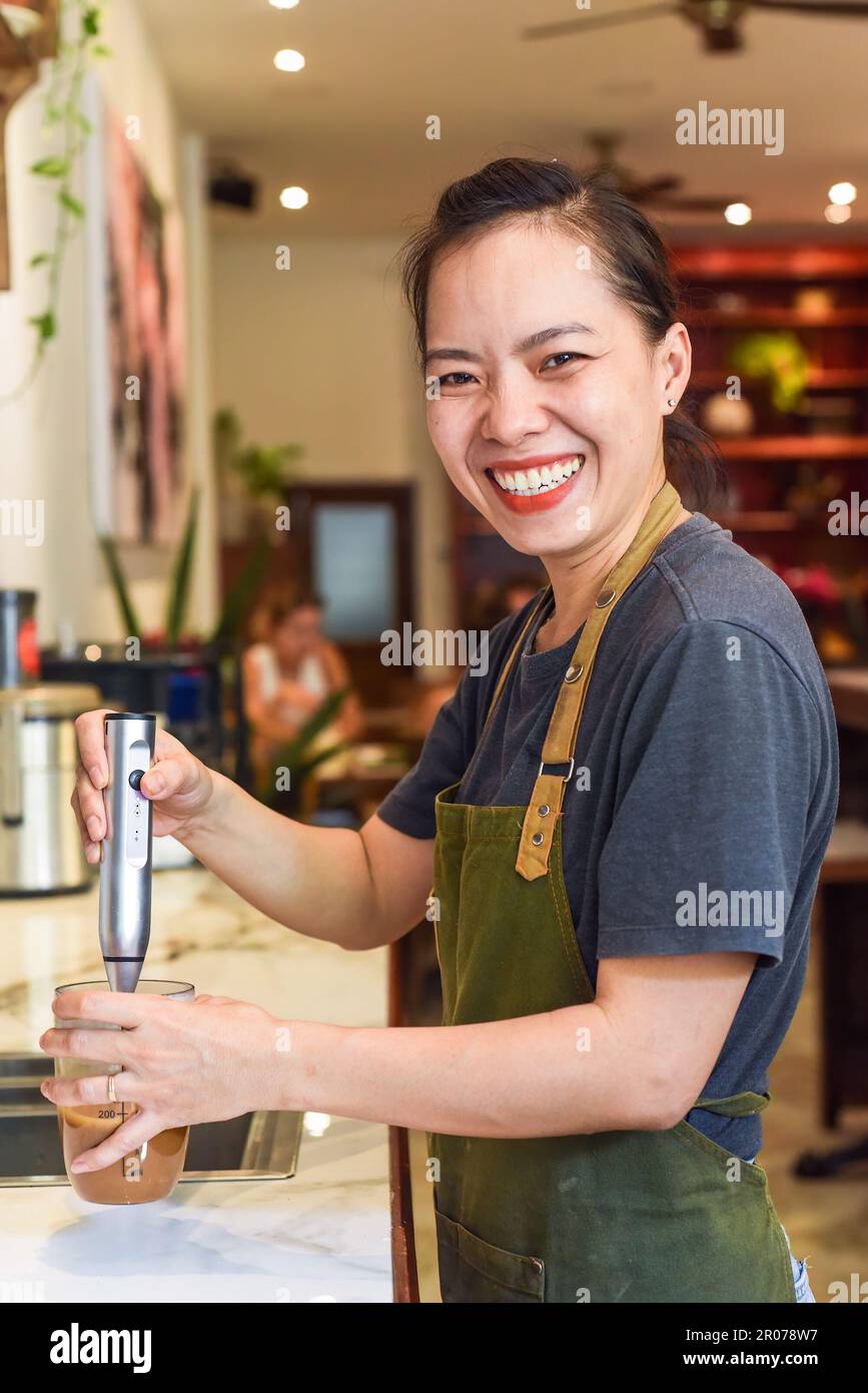 Barista vietnamien utilisant un batteur pour le lait condensé dans une tasse en verre pour préparer le café vietnamien SUA Banque D'Images