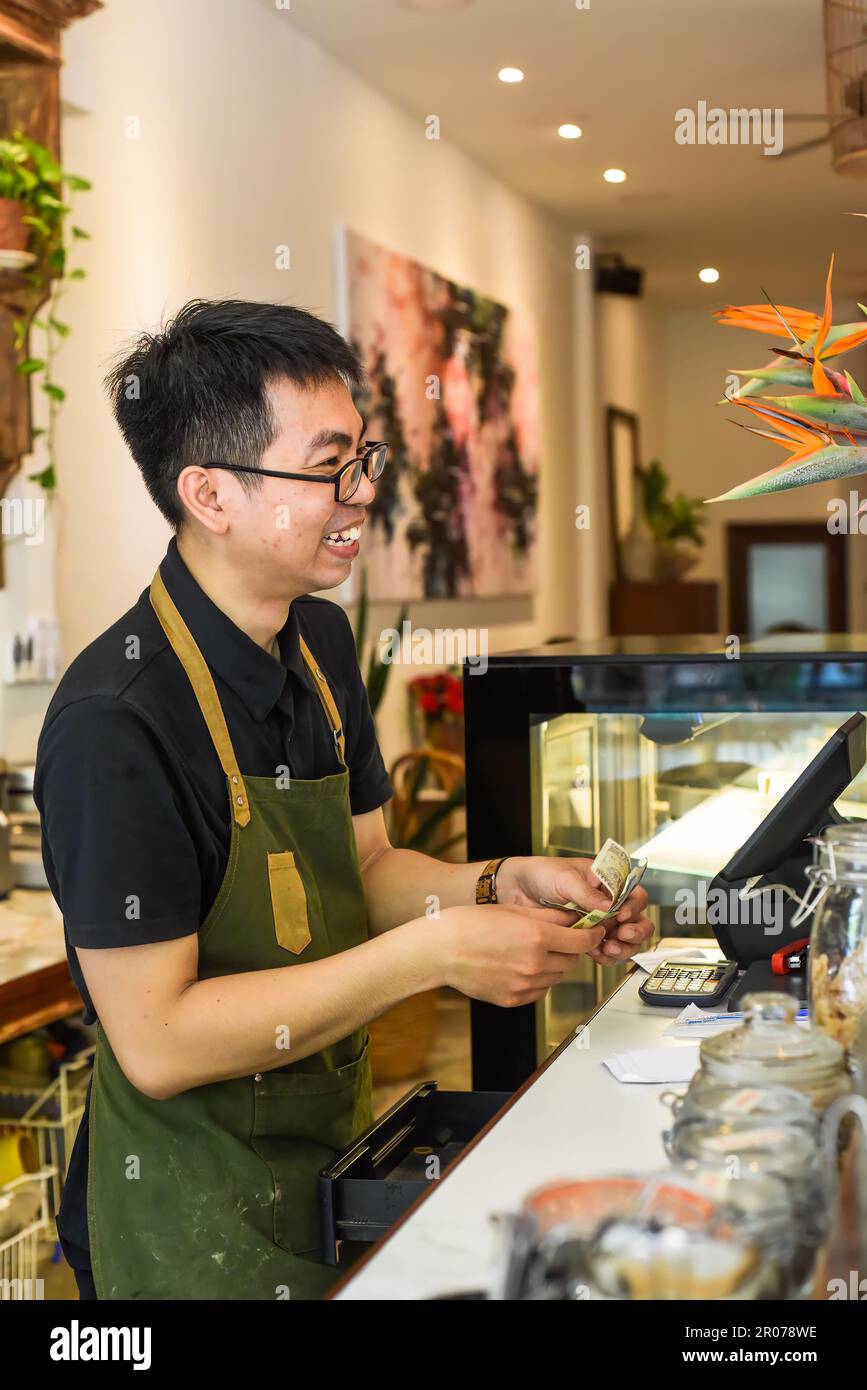Un serveur vietnamien travaillant au comptoir avec une machine à caisses dans un café Banque D'Images