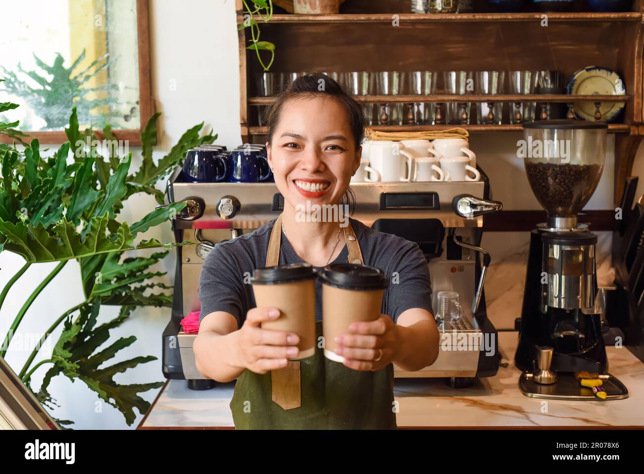 Une serveuse vietnamienne souriante tenant des tasses en papier avec du café dans un café Banque D'Images