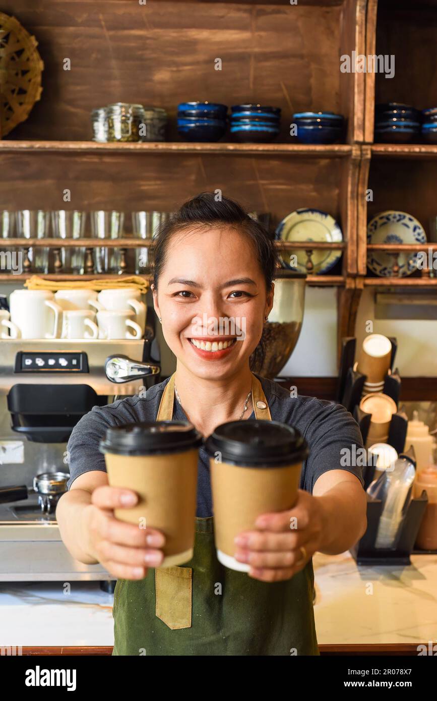 Une serveuse vietnamienne souriante tenant des tasses en papier avec du café dans un café Banque D'Images