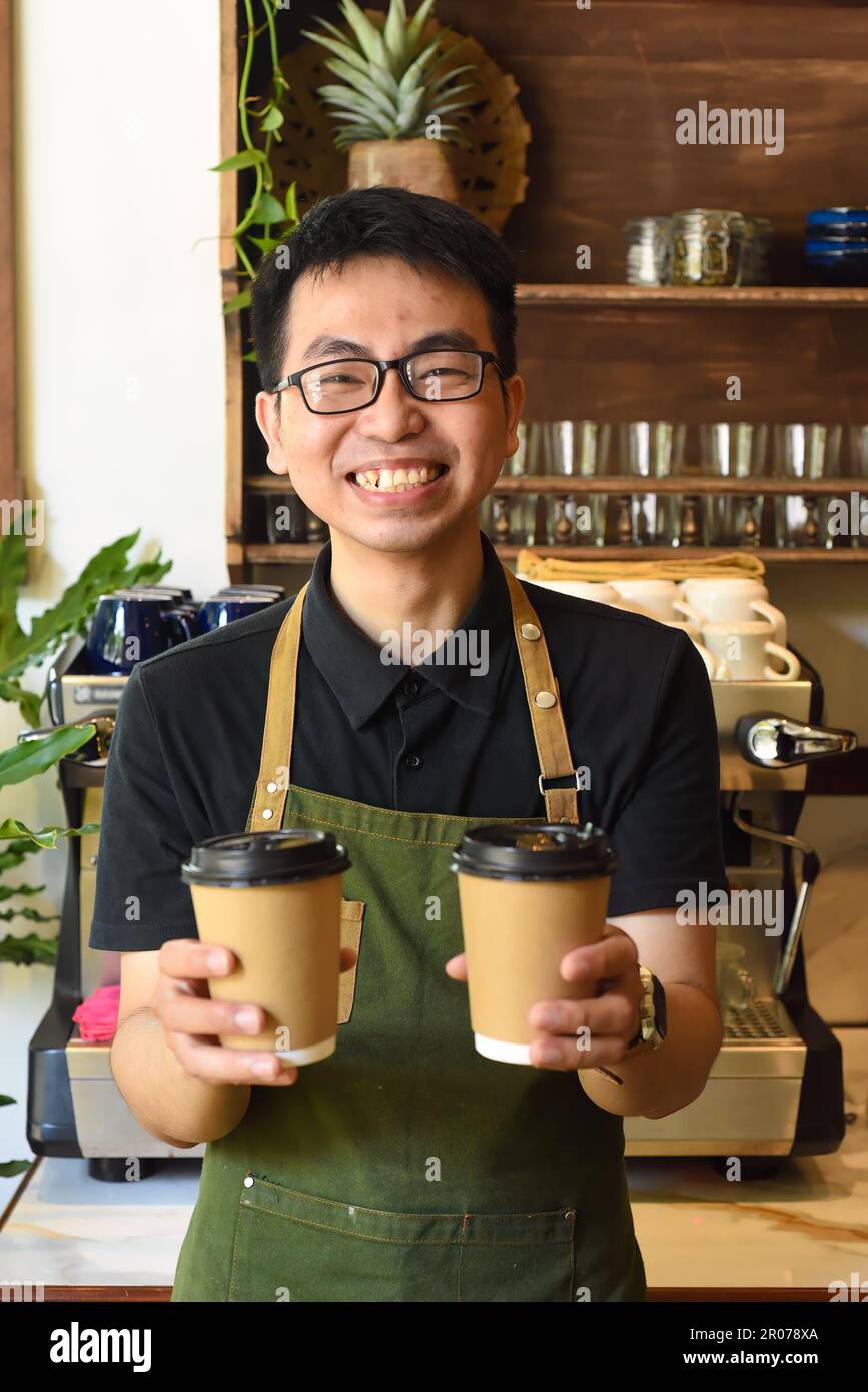Serveur vietnamien souriant tenant des tasses en papier avec du café dans un café Banque D'Images