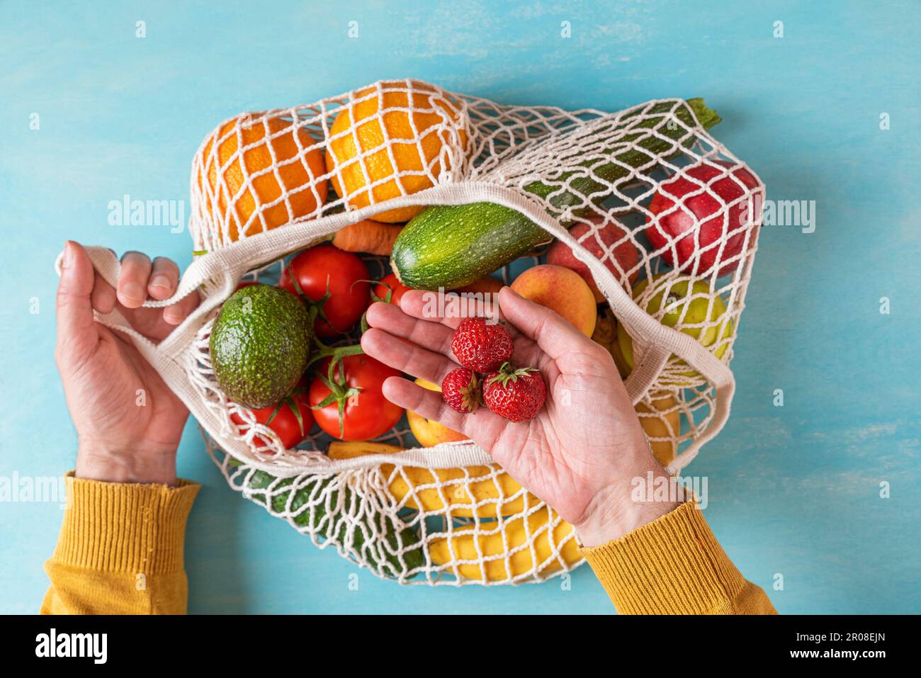 Homme poignet prenant des fraises du sac à provisions de filet avec des fruits et des légumes. Mode de vie durable, concept zéro déchet Banque D'Images