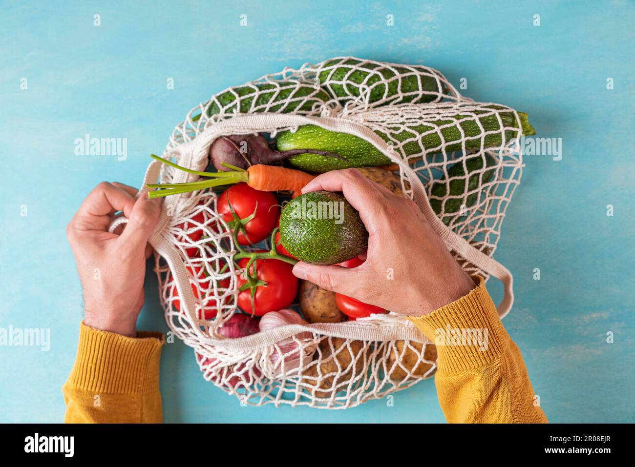 Homme à la main prenant des fruits de pêche du sac à provisions de filet avec des fruits et des légumes. Magasins écologiques Banque D'Images