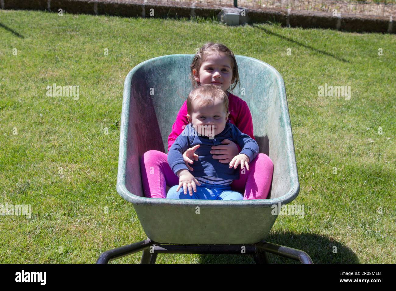 Image de deux adorables enfants souriants se tenant à l'intérieur d'une brouette. Amour fraternel comme ils jouent dans le jardin avec leur soeur de fabrication Banque D'Images