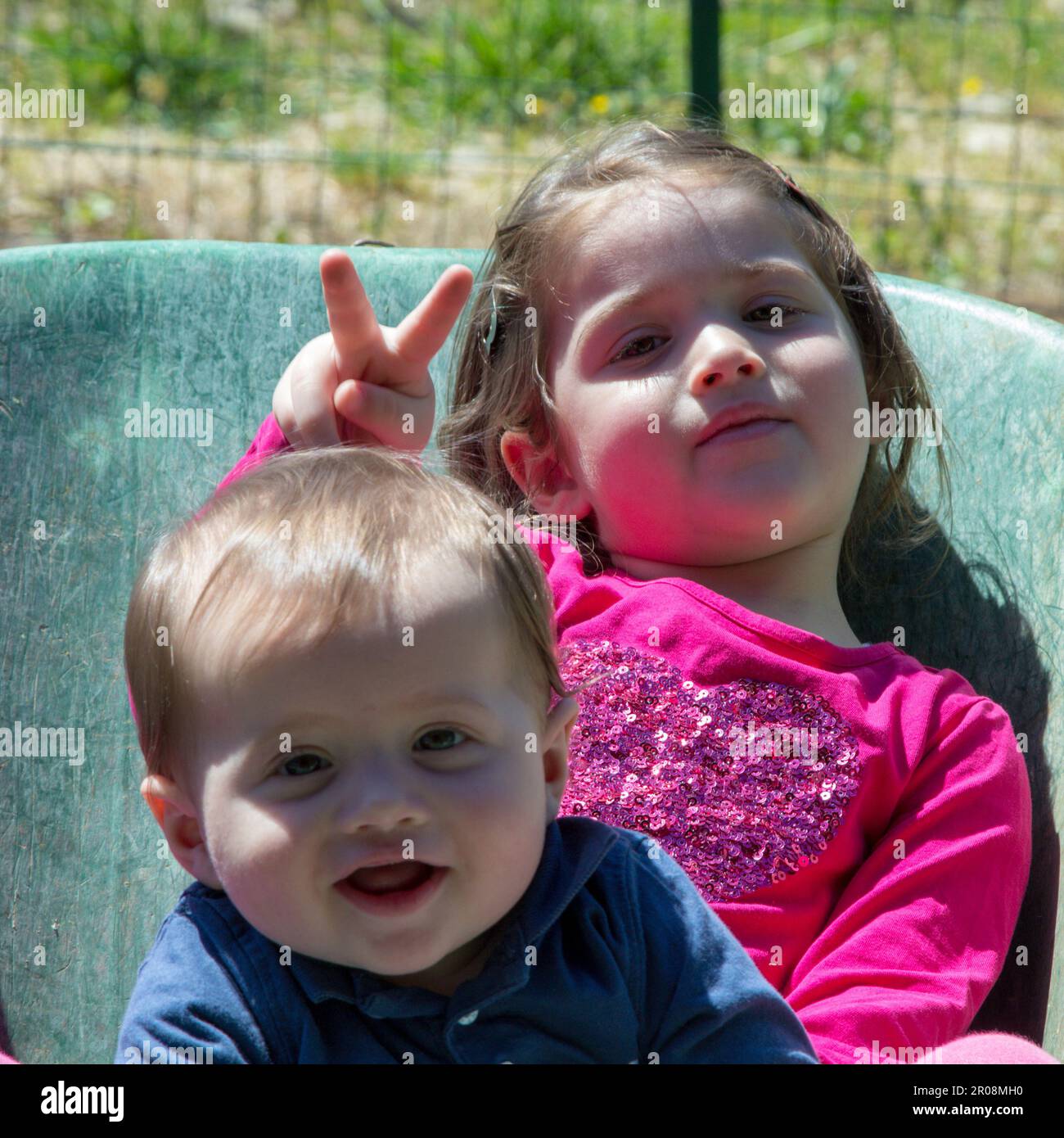 Image de deux adorables enfants souriants se tenant à l'intérieur d'une brouette. Amour fraternel comme ils jouent dans le jardin avec leur soeur de fabrication Banque D'Images