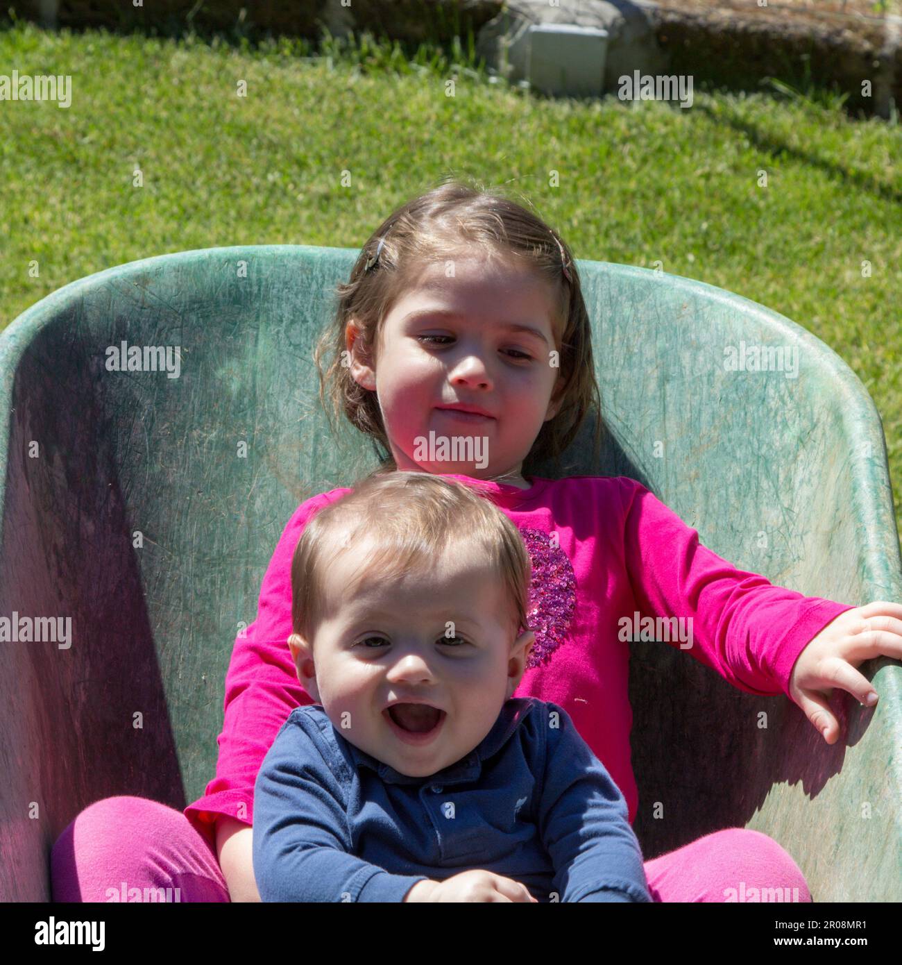 Image de deux adorables enfants souriants se tenant à l'intérieur d'une brouette. Amour fraternel comme ils jouent dans le jardin Banque D'Images