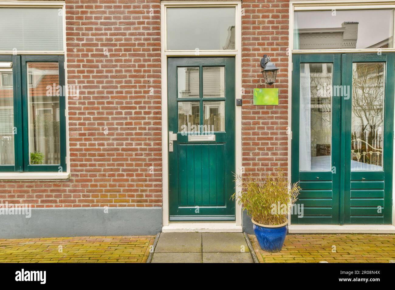 un bâtiment en briques avec deux portes vertes et un pot de fleurs bleues sur le trottoir devant la porte est vide Banque D'Images