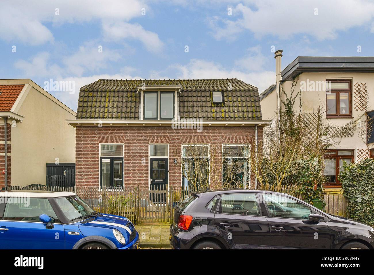 deux voitures garées l'une à côté de l'autre en face d'une rangée de maisons par une journée ensoleillée avec ciel bleu et nuages blancs Banque D'Images