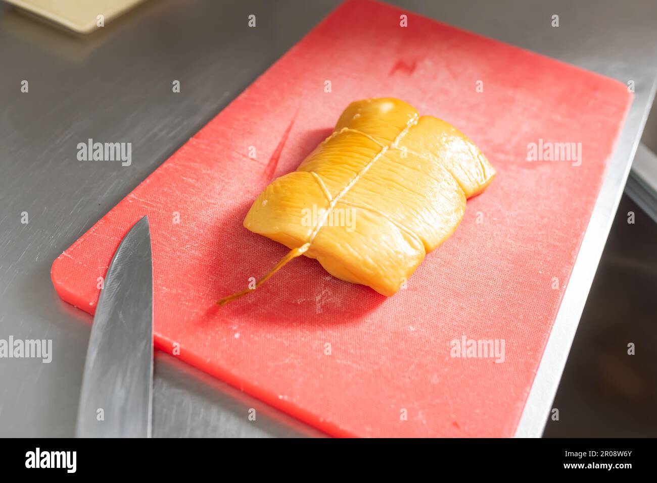 Le cuisinier coupe le calmar fumé pour les sushis sur un tableau rouge. Photo de haute qualité Banque D'Images