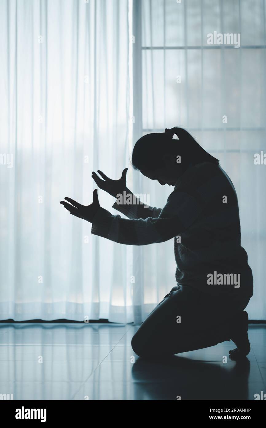 silhouette de femme s'agenouillant et priant dans une église moderne au coucher du soleil. L'adoration de prière catholique féminine à Dieu souhaite une meilleure vie à la maison à l'aube Banque D'Images