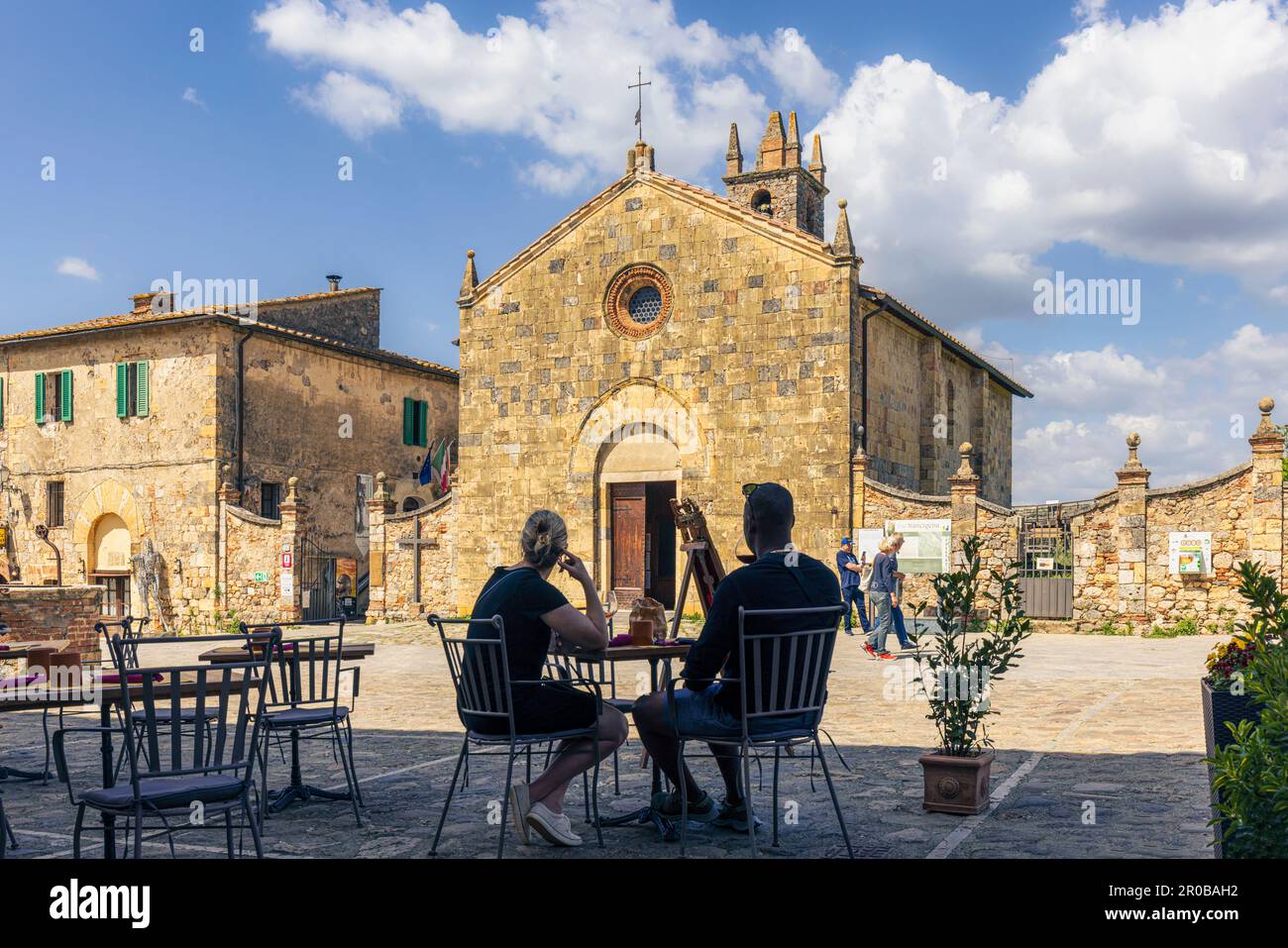 Monteriggioni, province de Sienne, Toscane, Italie. Un couple se régale d'un verre devant l'église romane-gothique de Santa Maria datant du 13th siècle. Banque D'Images