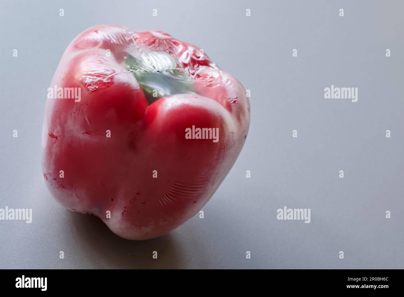 Poivron rouge scellé dans un emballage en plastique sur fond gris. Image dramatique d'un paprika d'un supermarché emballé dans du papier d'aluminium plastique. Zéro plastique. Banque D'Images