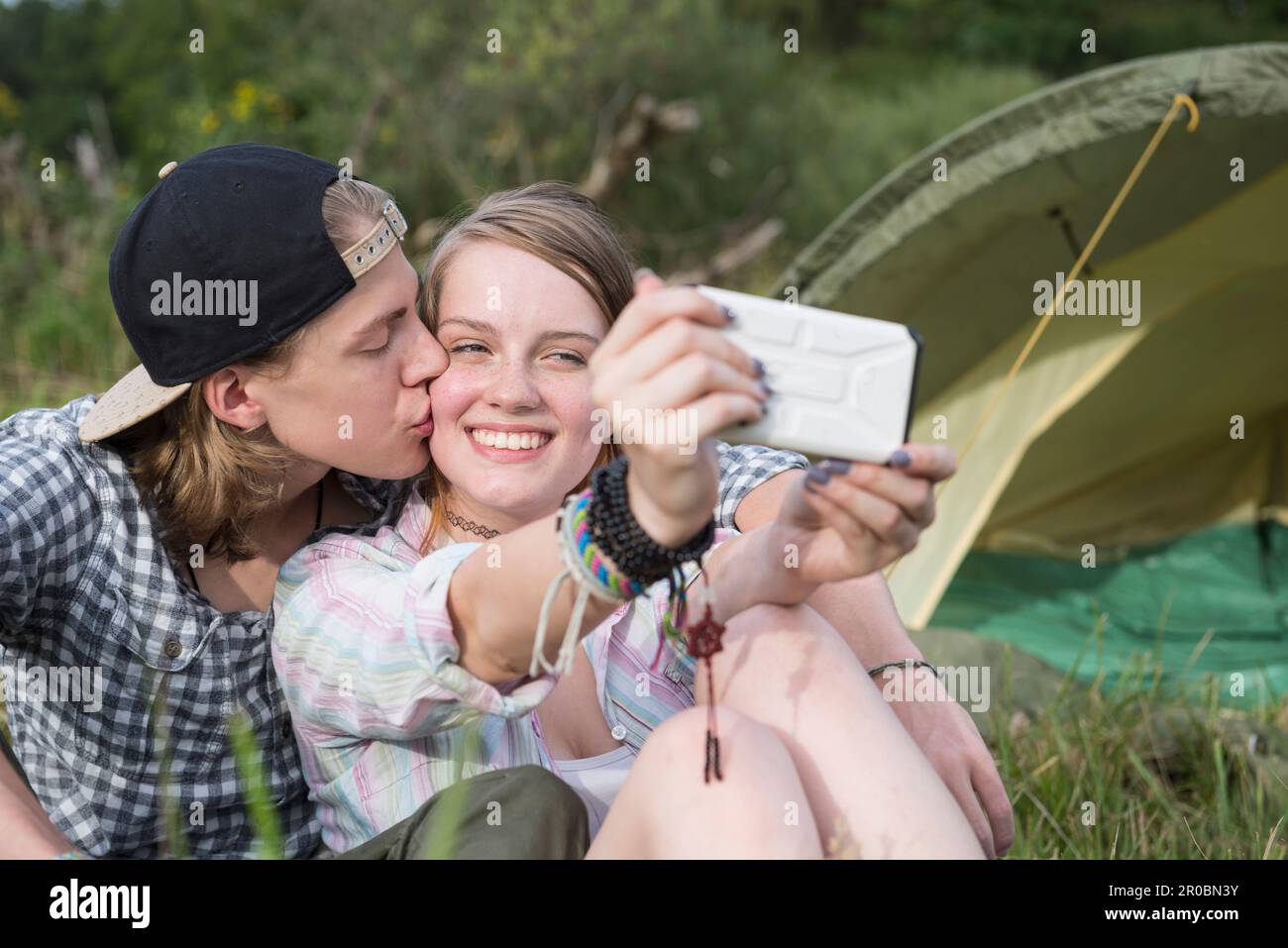 Un jeune couple embrasse et prend le selfie avec un smartphone devant la tente du camp, en Bavière, en Allemagne Banque D'Images