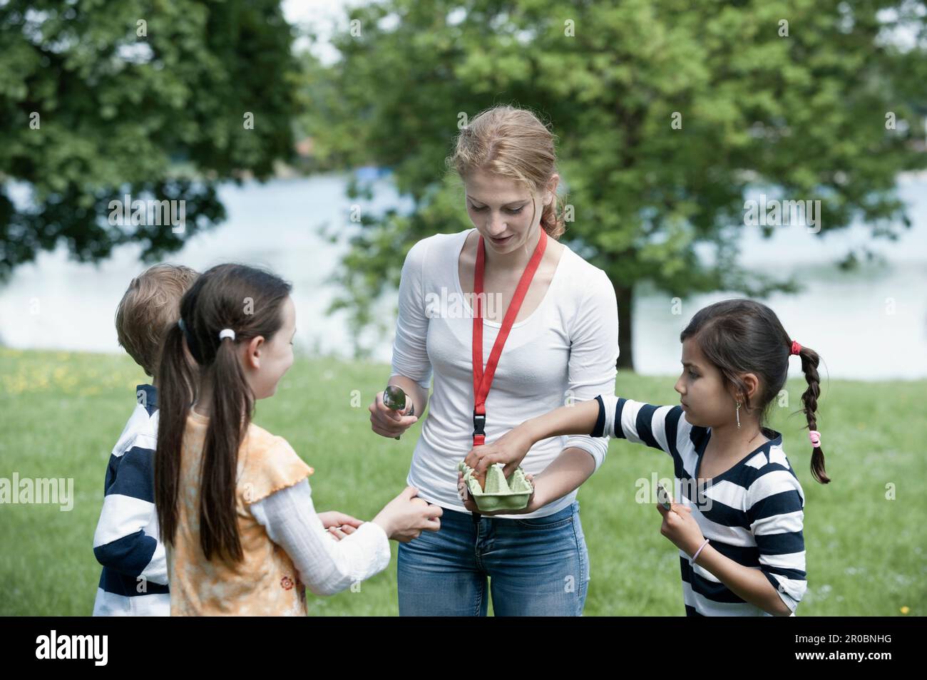 Femme entraîneur distribuant des oeufs aux enfants pour la course de cuillère dans un parc, Munich, Bavière, Allemagne Banque D'Images