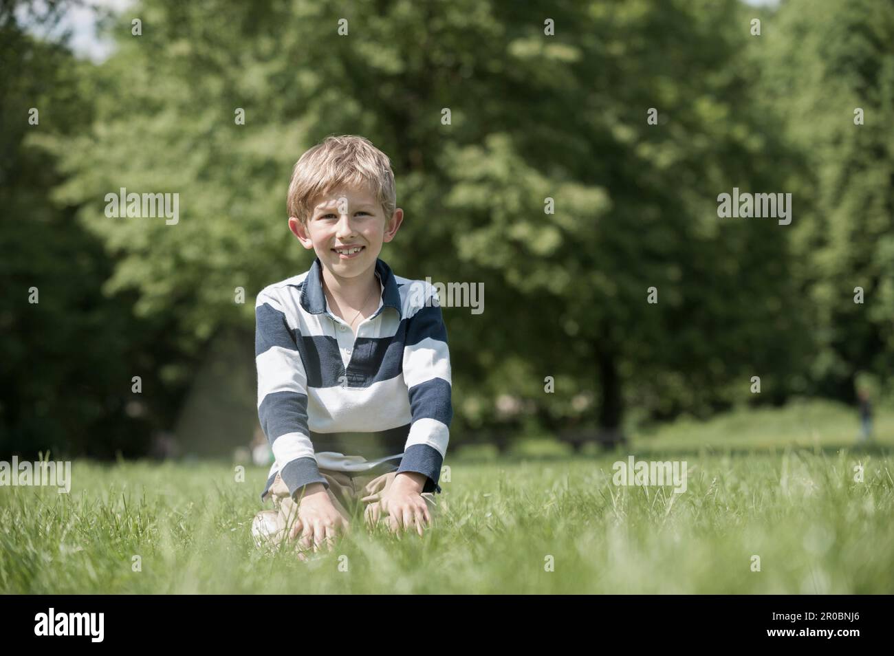 Garçon souriant et assis sur un terrain dans le parc, Munich, Bavière, Allemagne Banque D'Images