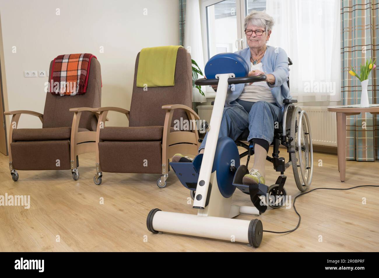 Femme âgée en fauteuil roulant s'exerçant sur un vélo d'exercice dans une maison de repos Banque D'Images