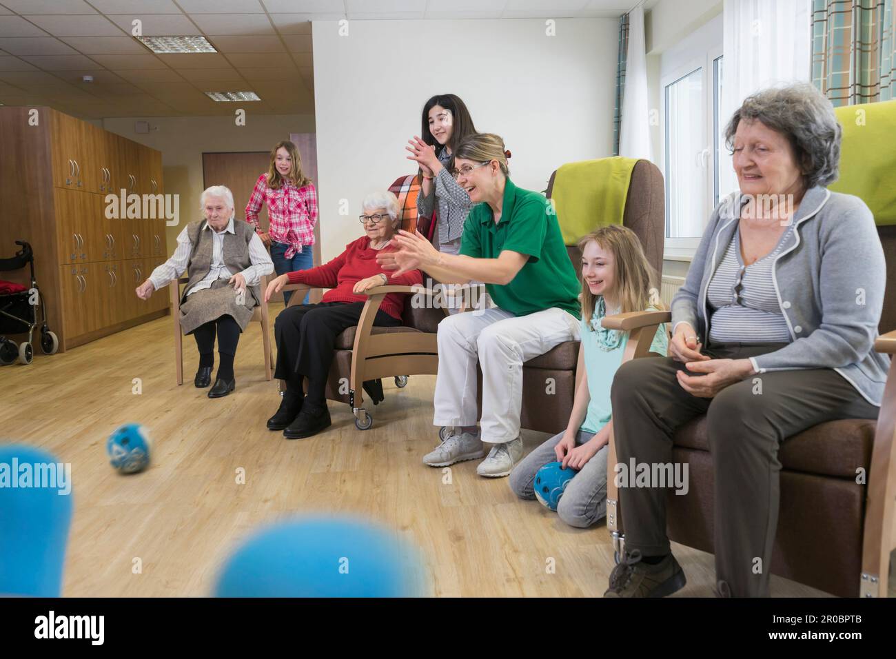 Filles jouant au bowling avec une infirmière et des femmes âgées dans la maison de repos Banque D'Images