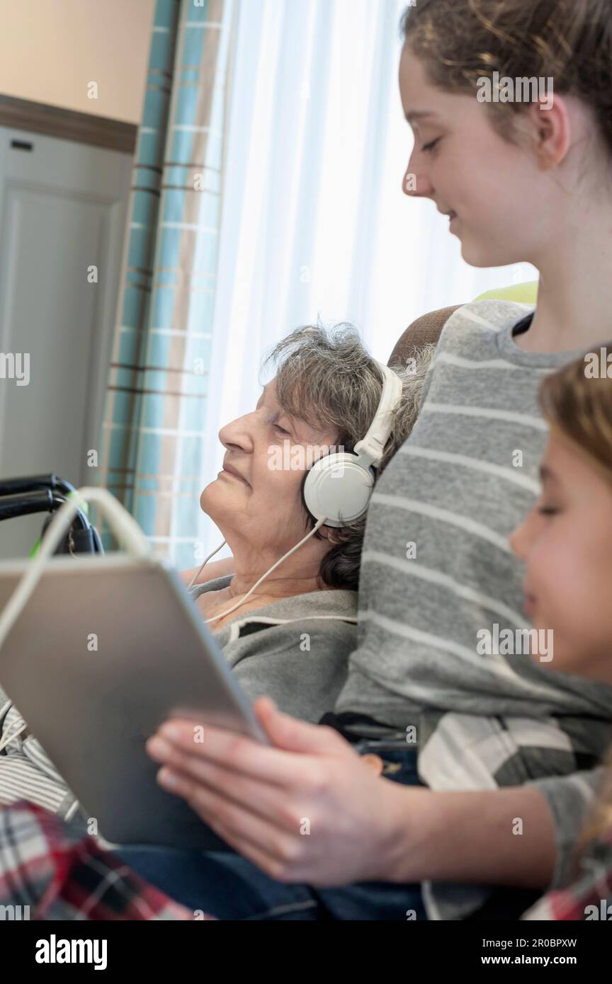 Femme âgée listant de la musique avec de grands enfants dans la maison de repos Banque D'Images