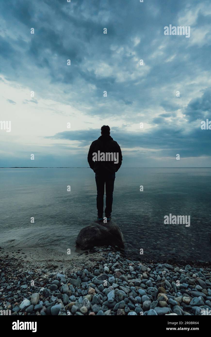 Silhouette d'homme debout seul sur un rocher dans l'eau au crépuscule. Banque D'Images