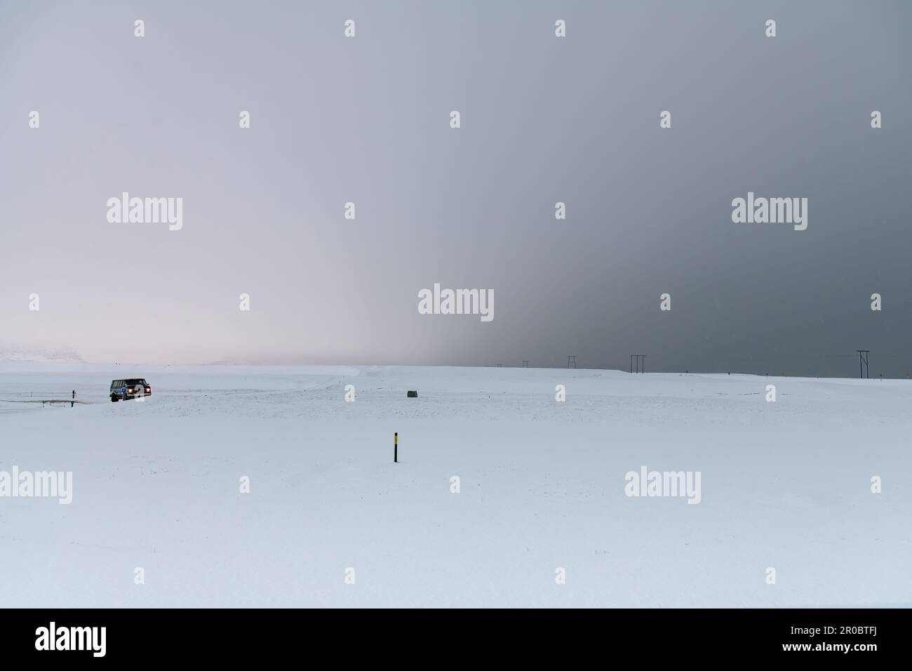 Vue panoramique sur un paysage de neige blanche presque plate et stérile en Islande avec une voiture sur une route invisible et une couleur de ciel allant du gris clair au gris foncé Banque D'Images