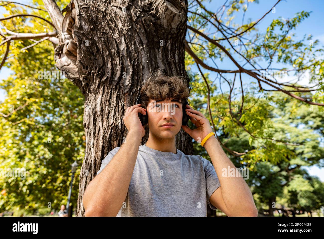 Beau jeune homme s'appuyant sur un arbre tout en écoutant de la musique Banque D'Images