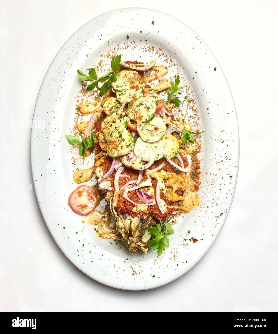 Un plat fraîchement cuit avec du poisson blanc succulent et une variété de légumes colorés, présenté sur une assiette blanche et garni d'herbes Banque D'Images