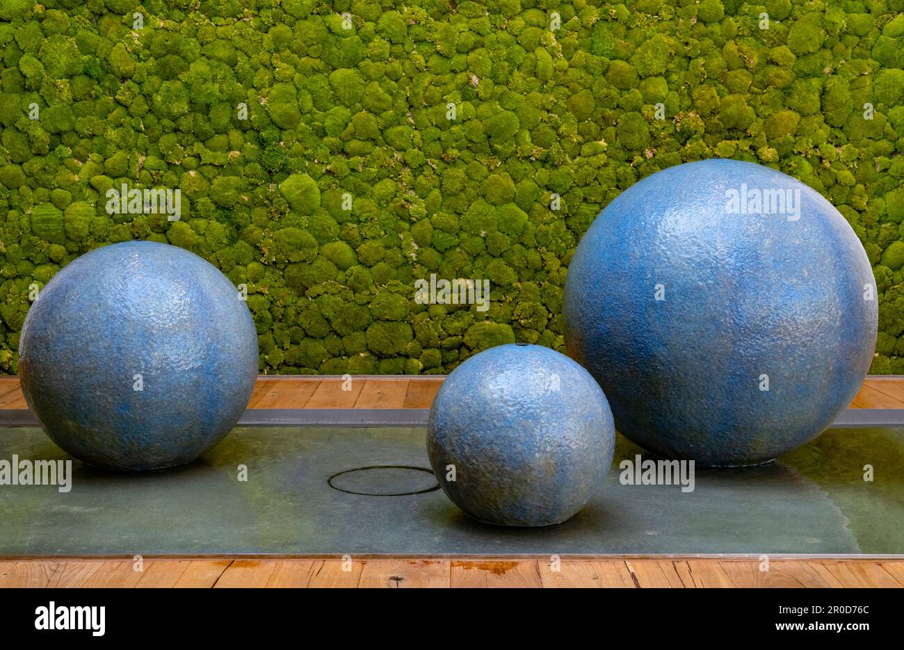 Fontaine sphérique flottante avec sphères bleues devant un mur vert moussy Banque D'Images