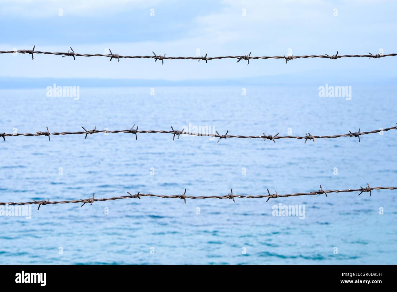 Gros plan sur la barrière barbelée contre la mer et le fond bleu du ciel. Le barbelé métaphorique est comme les frontières et les obstacles dans le cerveau. Banque D'Images