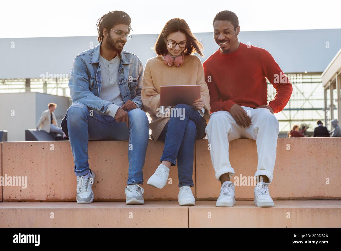 Des étudiants joyeux du millénaire noirs, arabes et européens regardant des cours en ligne sur tablette sur le campus Banque D'Images