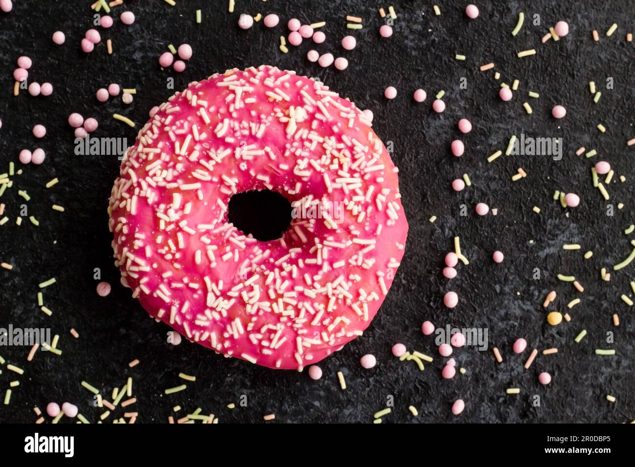 Les beignets sucrés de couleur rose sont conçus avec des bonbons de décoration sur une surface noire. Banque D'Images