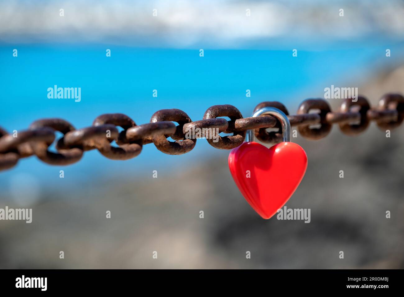 Un unique cadenas rouge, non marqué, en forme de coeur, d'amour ou d'amour attaché à une chaîne épaisse par des amoureux pour symboliser leur affection ou leur amour Banque D'Images