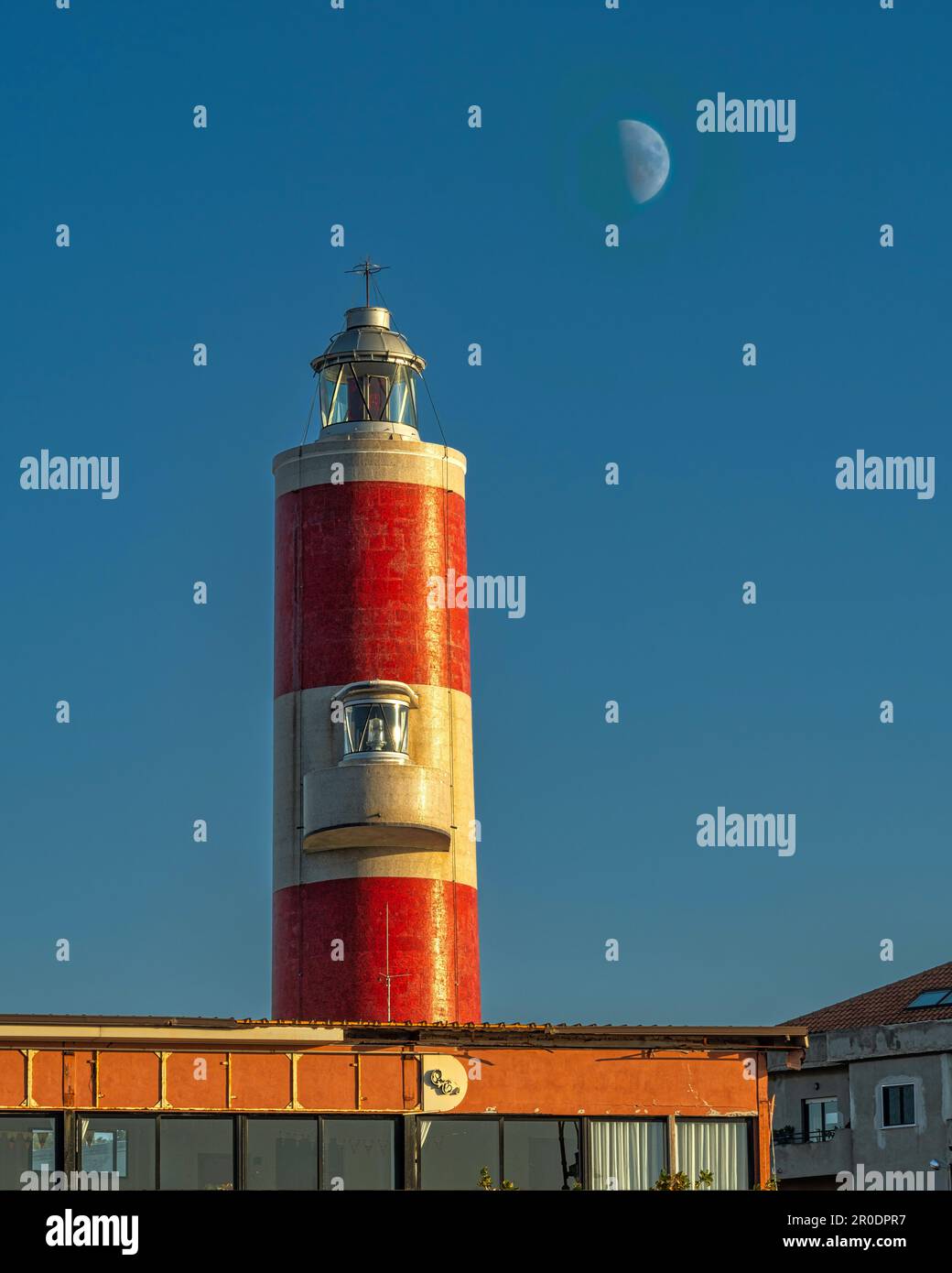 Phare de Punta Pezzo avec des bandes rouges et blanches illuminées par le coucher du soleil avec la lune en arrière-plan. Villa San Giovanni, Calabre Banque D'Images
